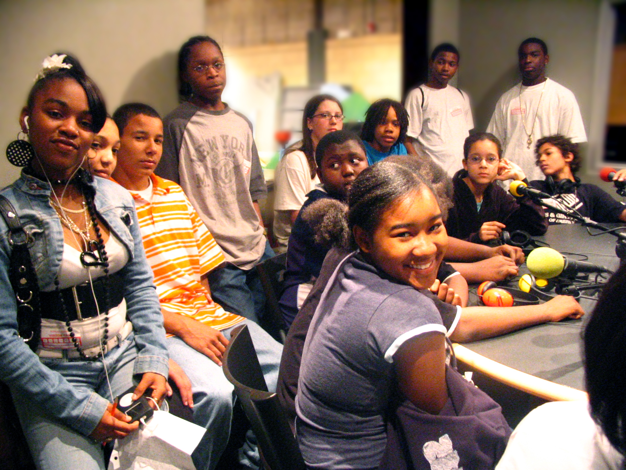 Twelve youth sitting around microphones on a table in a radio studio