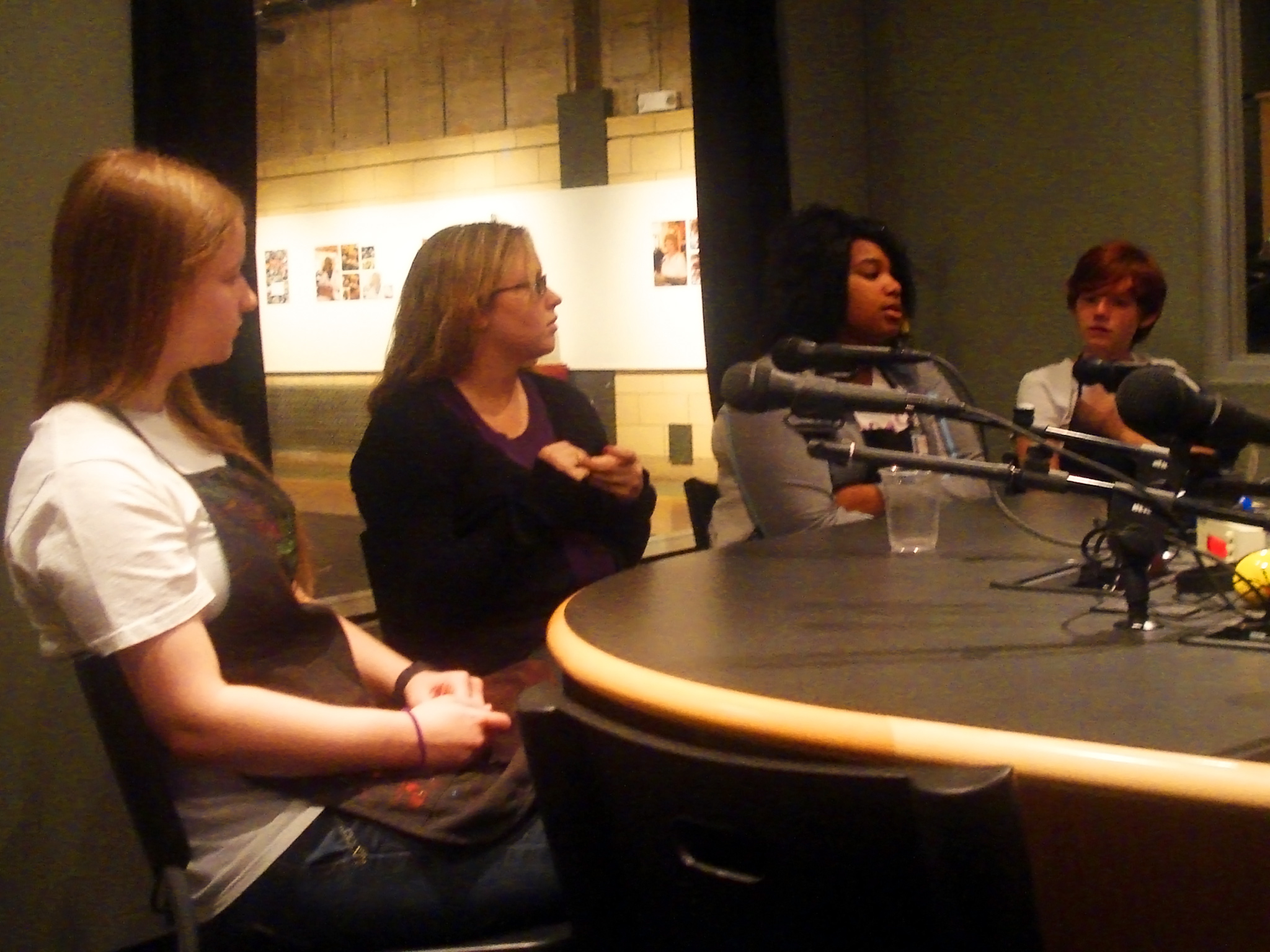 Four individuals sitting behind microphones in a radio studio