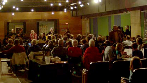 newlanders2 An audience of people watching adults speaking into microphones in front of a radio studio
