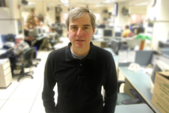 An adult wearing a black sweater standing in an office