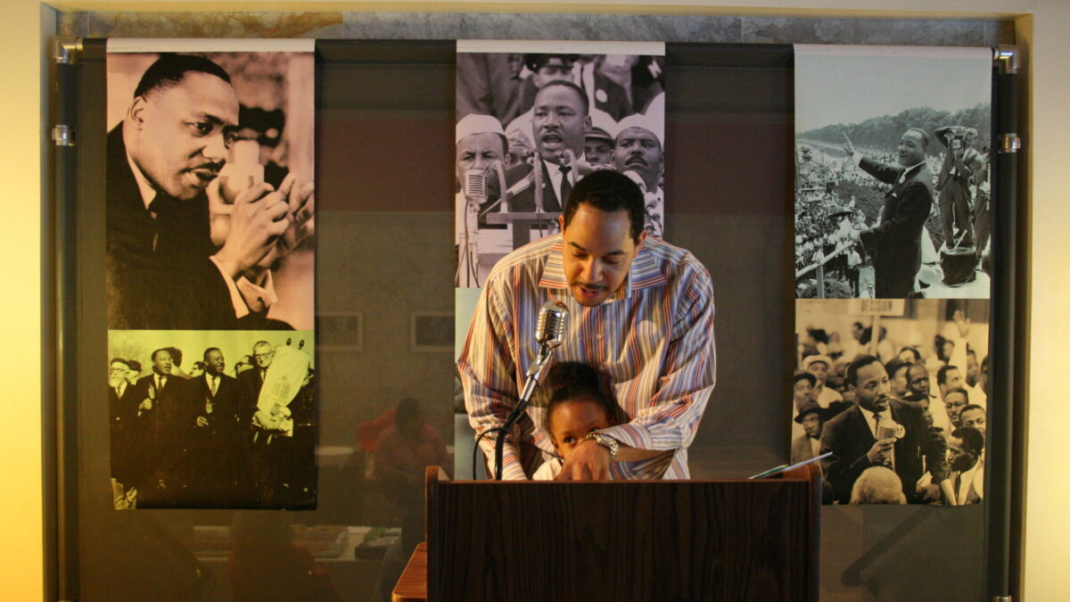 A youth and an adult standing behind a podium speaking into a microphone in front of banners of Martin Luther King, Jr.