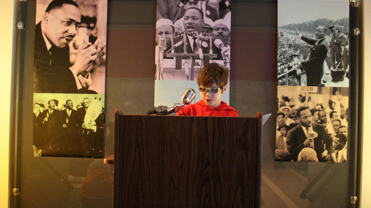 A youth standing behind a podium speaking into a microphone in front of banners of Martin Luther King, Jr.
