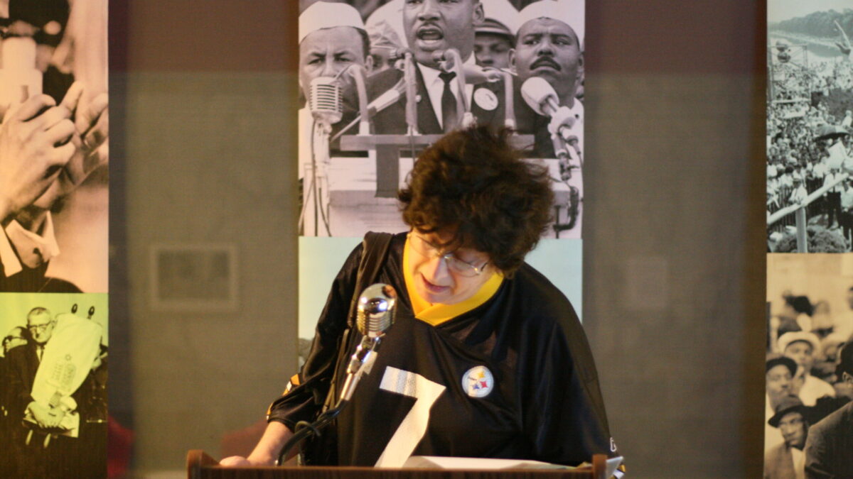 An adult standing behind a podium speaking into a microphone in front of banners of Martin Luther King, Jr.