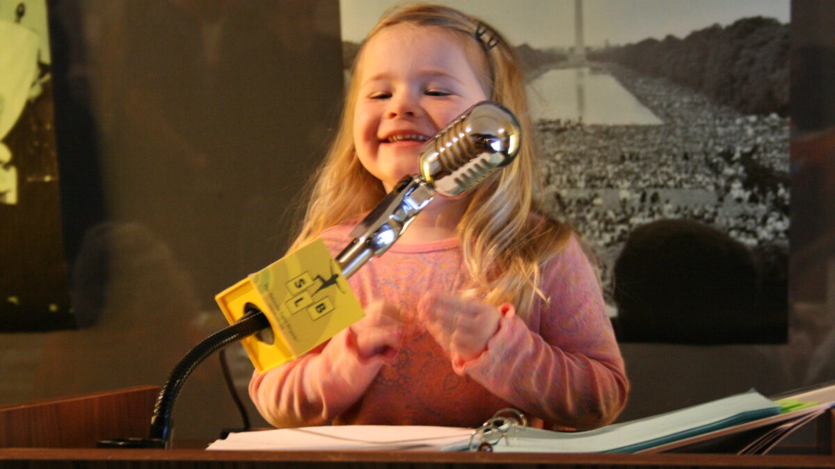 A youth standing behind a podium speaking into a microphone in front of banners of Martin Luther King, Jr.