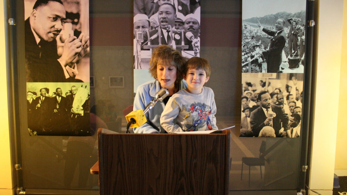 Two youth standing behind a podium speaking into a microphone in front of banners of Martin Luther King, Jr.