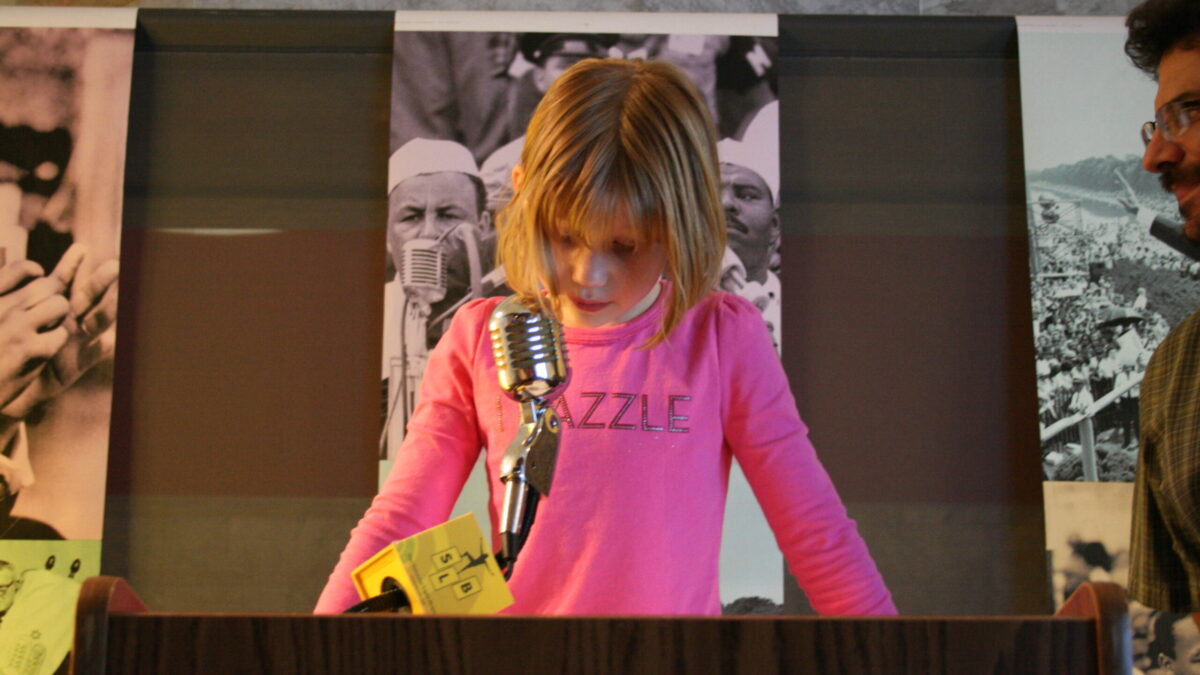 A youth standing behind a podium speaking into a microphone in front of banners of Martin Luther King, Jr.