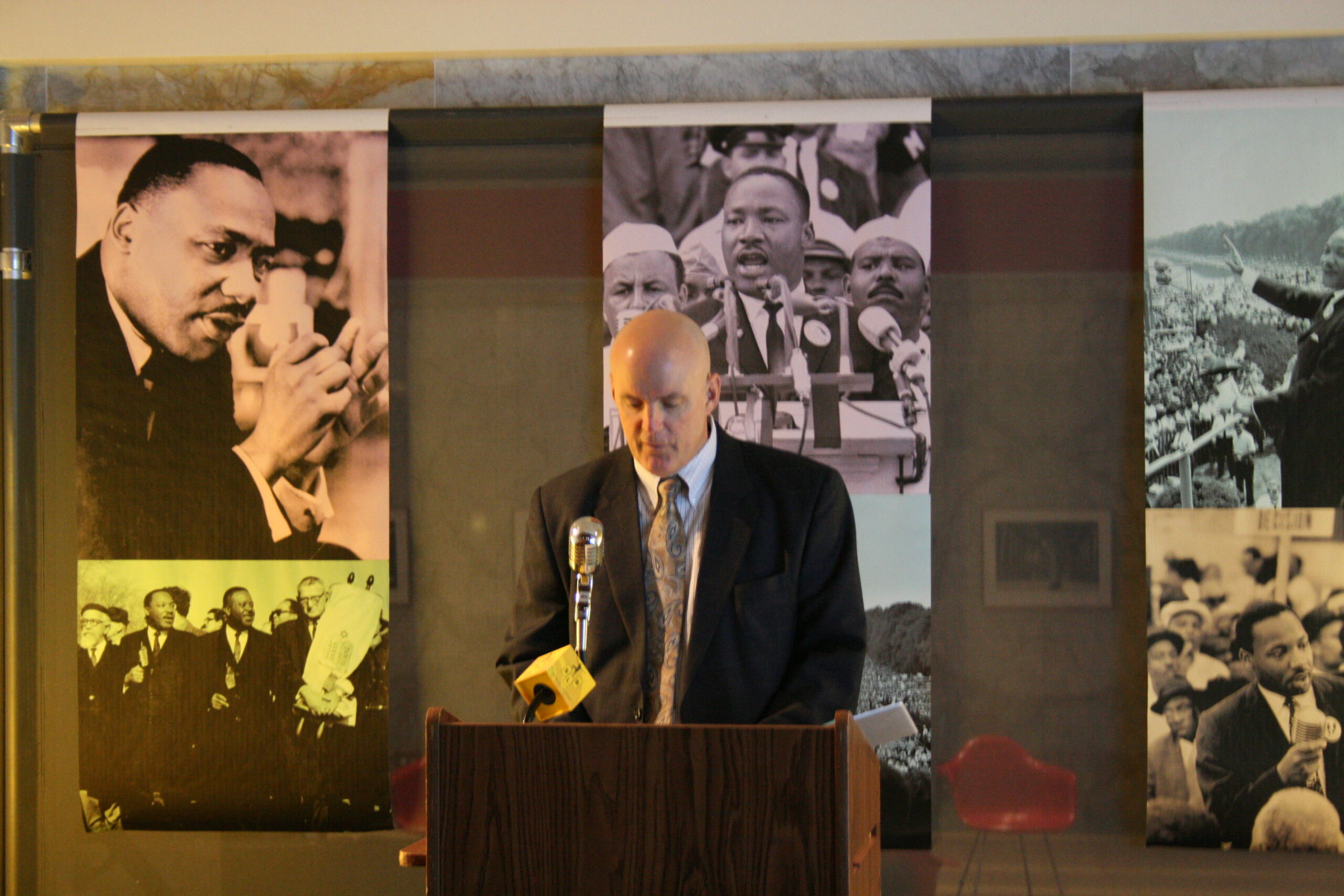 An adult standing behind a podium speaking into a microphone in front of banners of Martin Luther King, Jr.