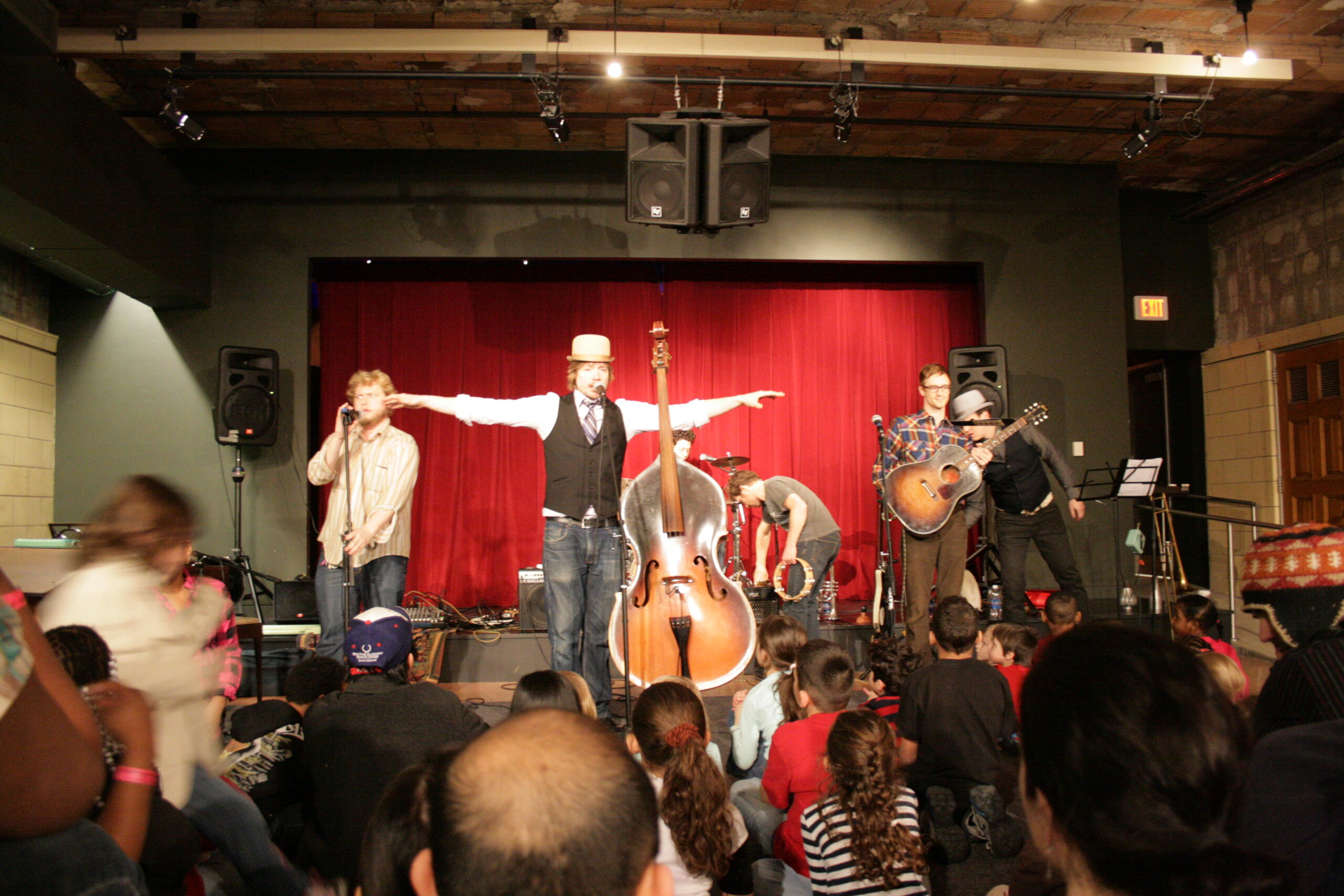 Five adults playing string instruments for a crowd of children