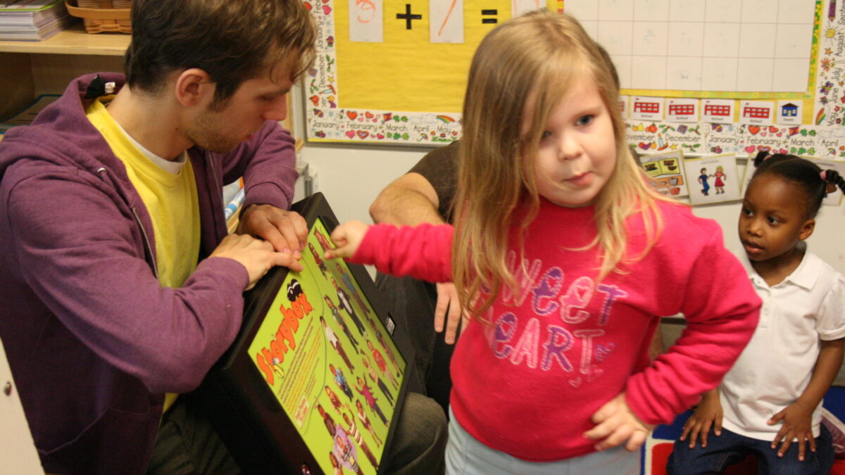 An adult and a youth interacting with a tablet in a classroom