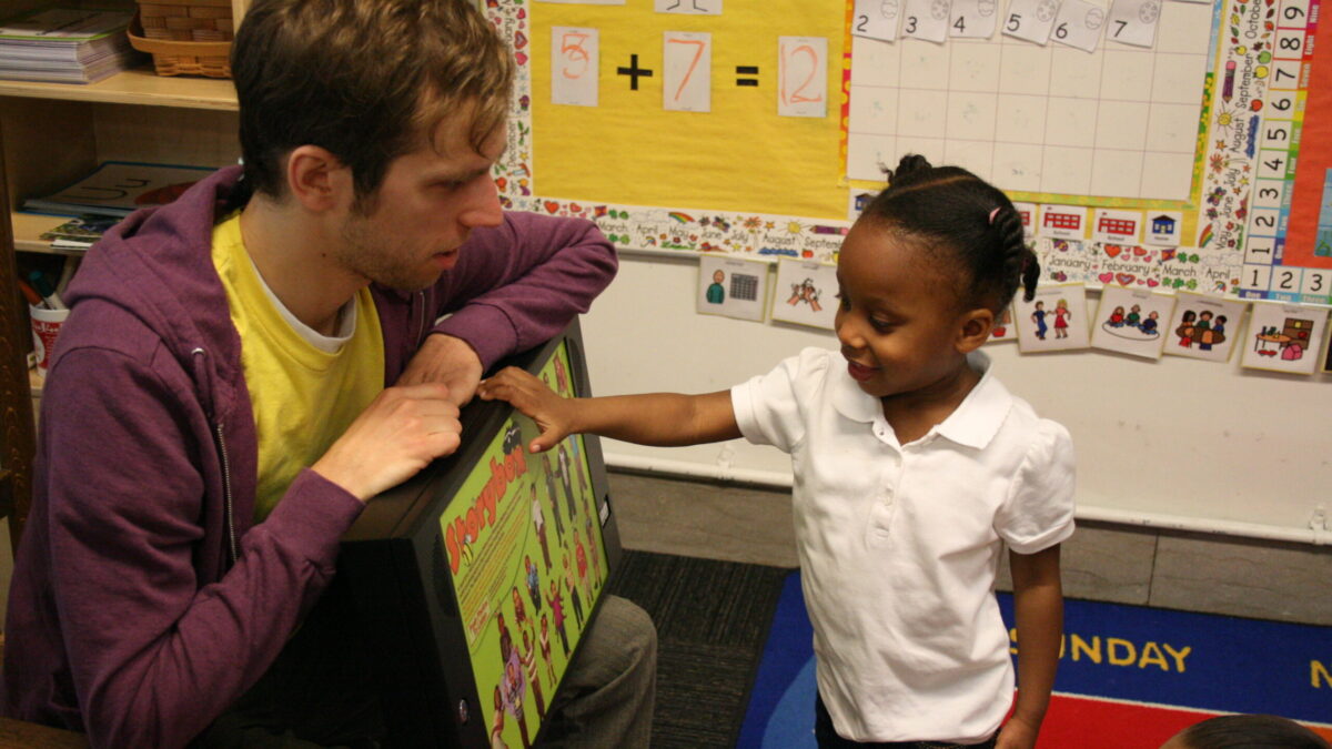 An adult and a youth interacting with a tablet in a classroom