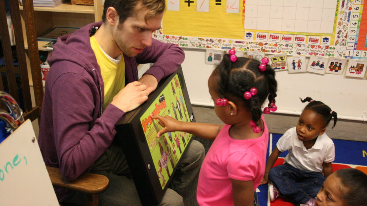 An adult and a youth interacting with a tablet in a classroom
