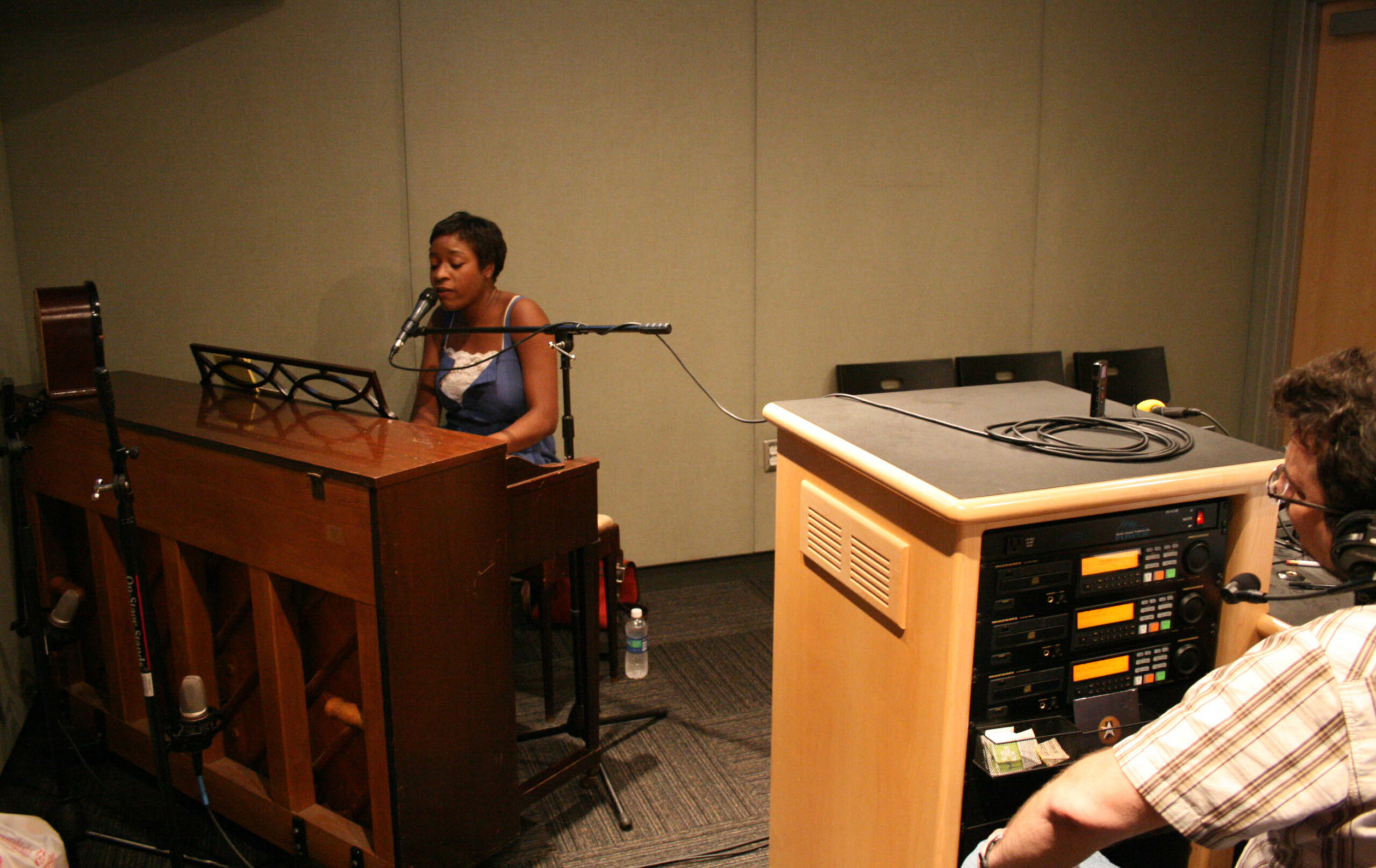 An adult playing a piano and singing into a microphone in a radio studio