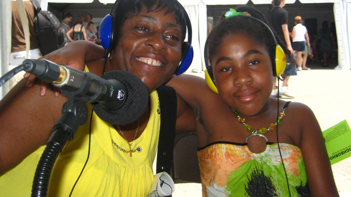 Two individuals, one wearing headphones, smiling and standing behind a microphone