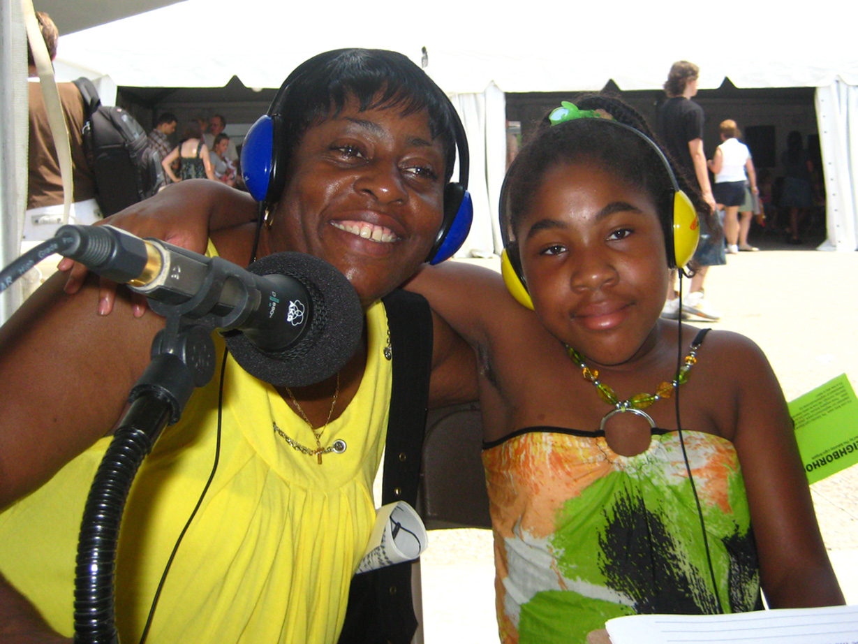 Two individuals, one wearing headphones, smiling and standing behind a microphone