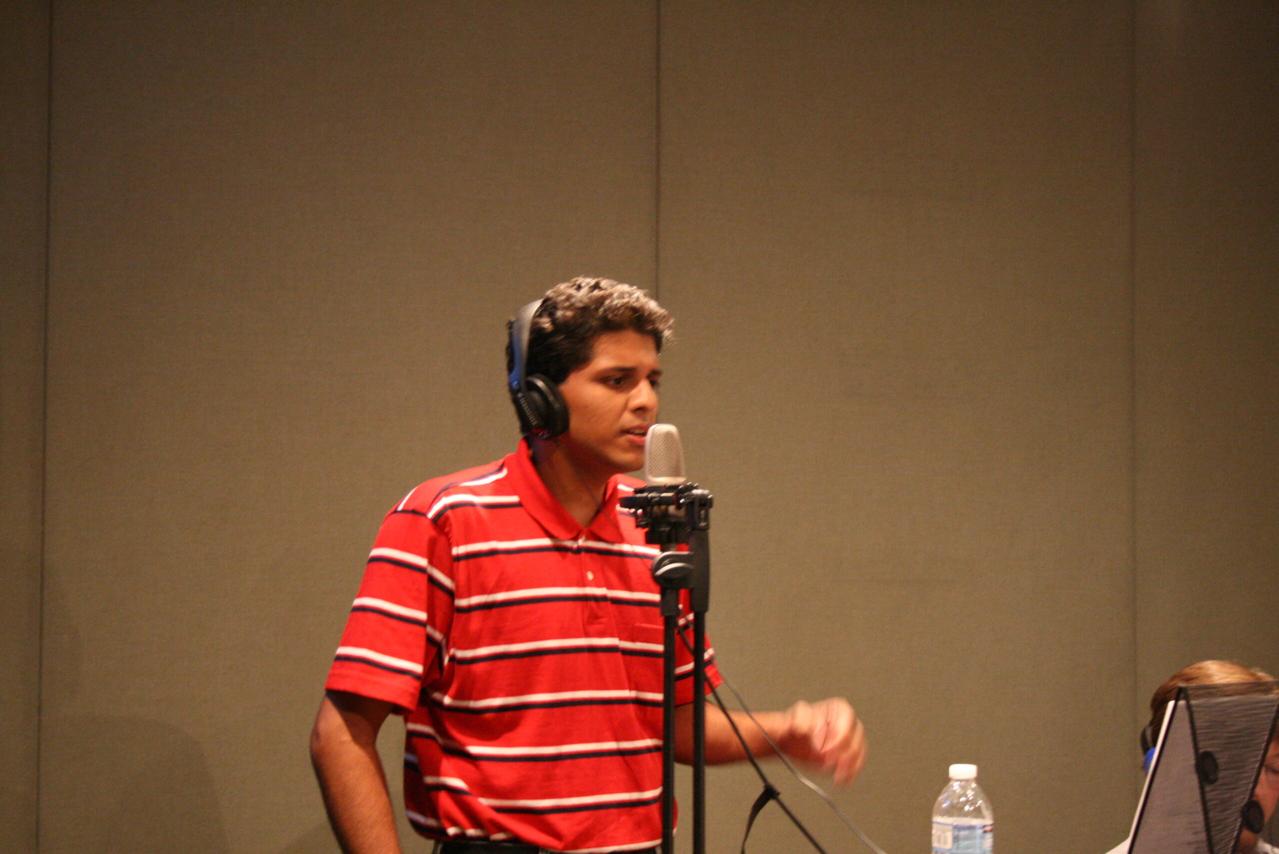 A teen wearing headphones singing into a microphone in a radio studio