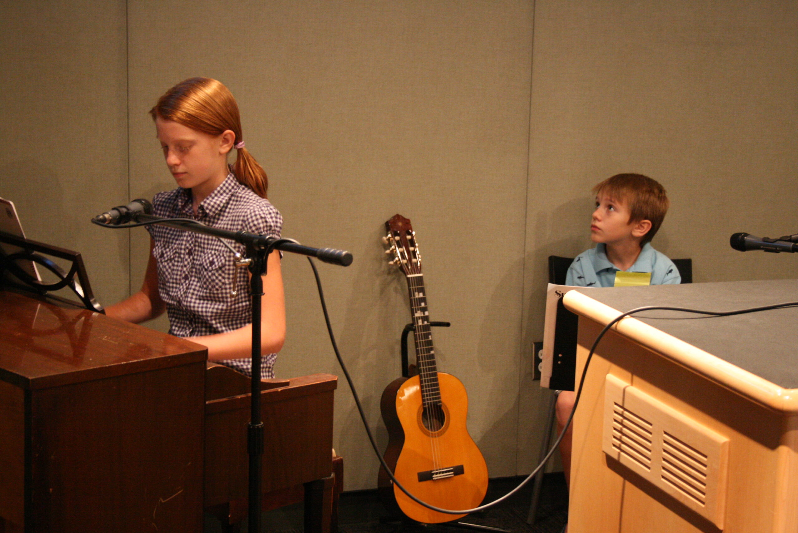 A youth playing a piano and a youth sitting and looking at the wall in a radio studio