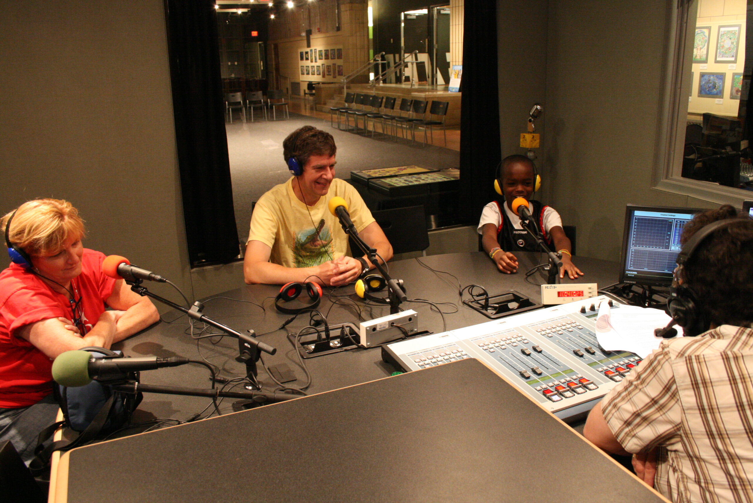 Two adults and a youth wearing headphones speaking into microphones in a radio studio