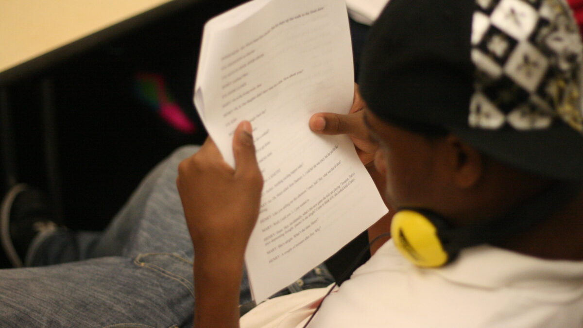 A youth wearing headphones around their neck holding a piece of paper in a classroom