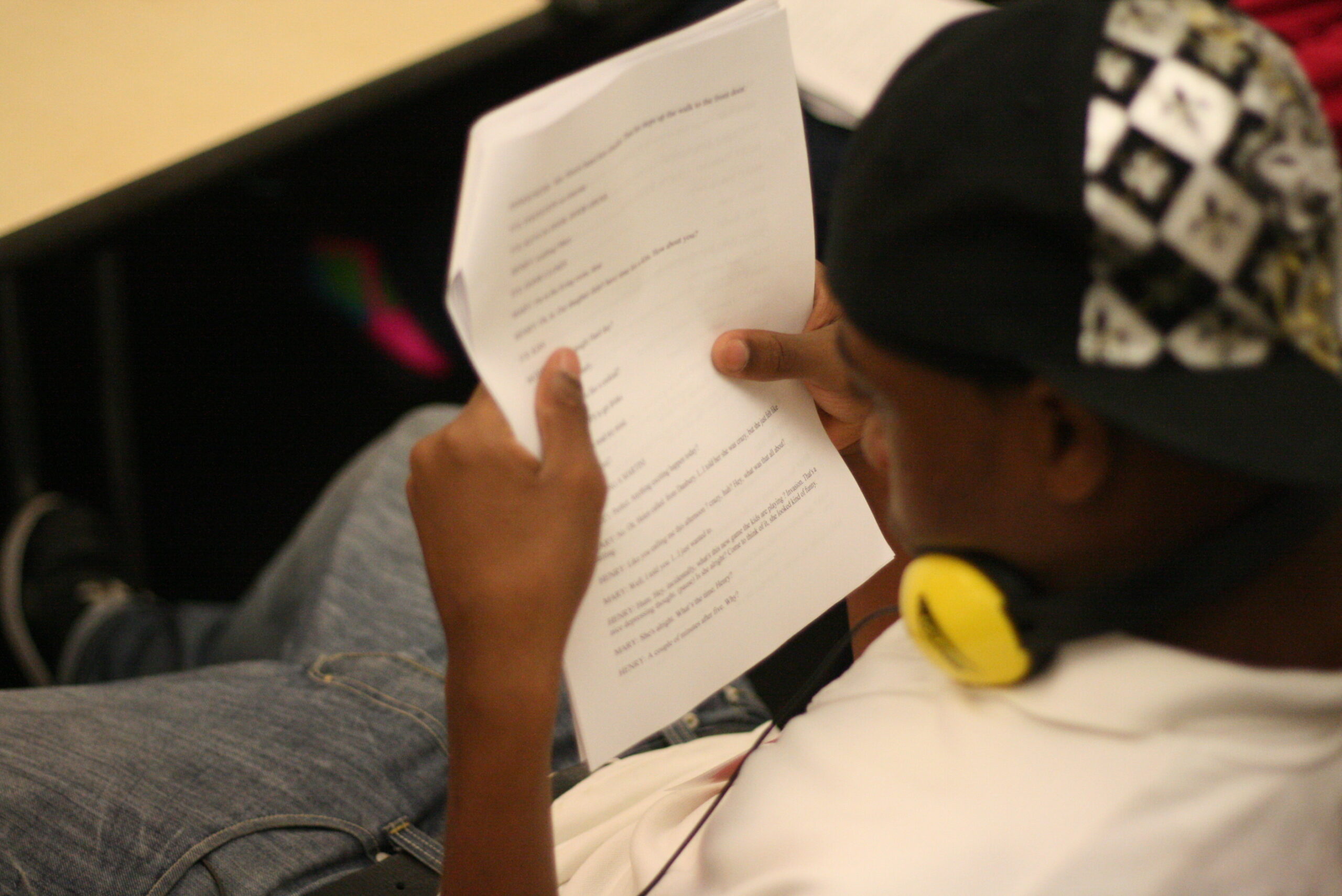 A youth wearing headphones around their neck holding a piece of paper in a classroom
