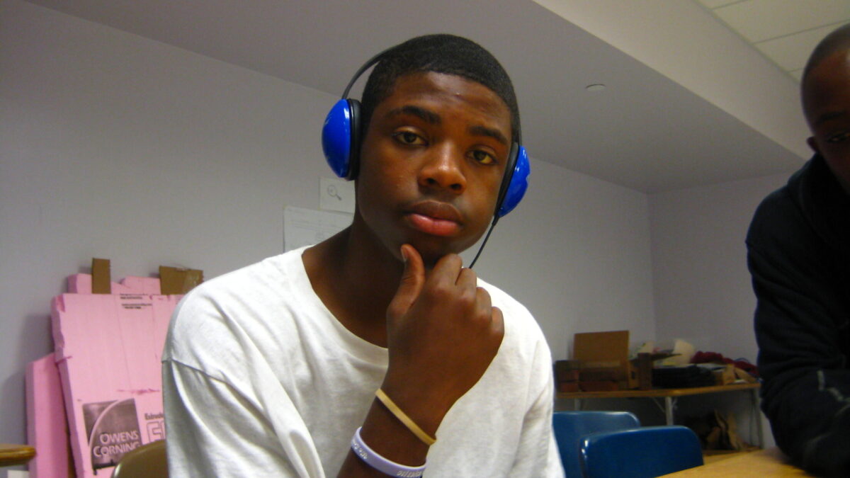 A teen wearing headphones posing at a classroom desk