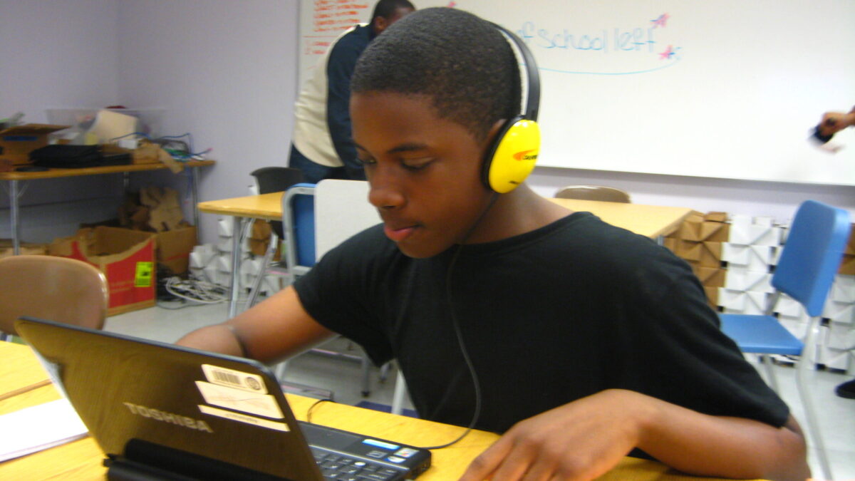 A teen wearing headphones looking at a laptop computer in a classroom