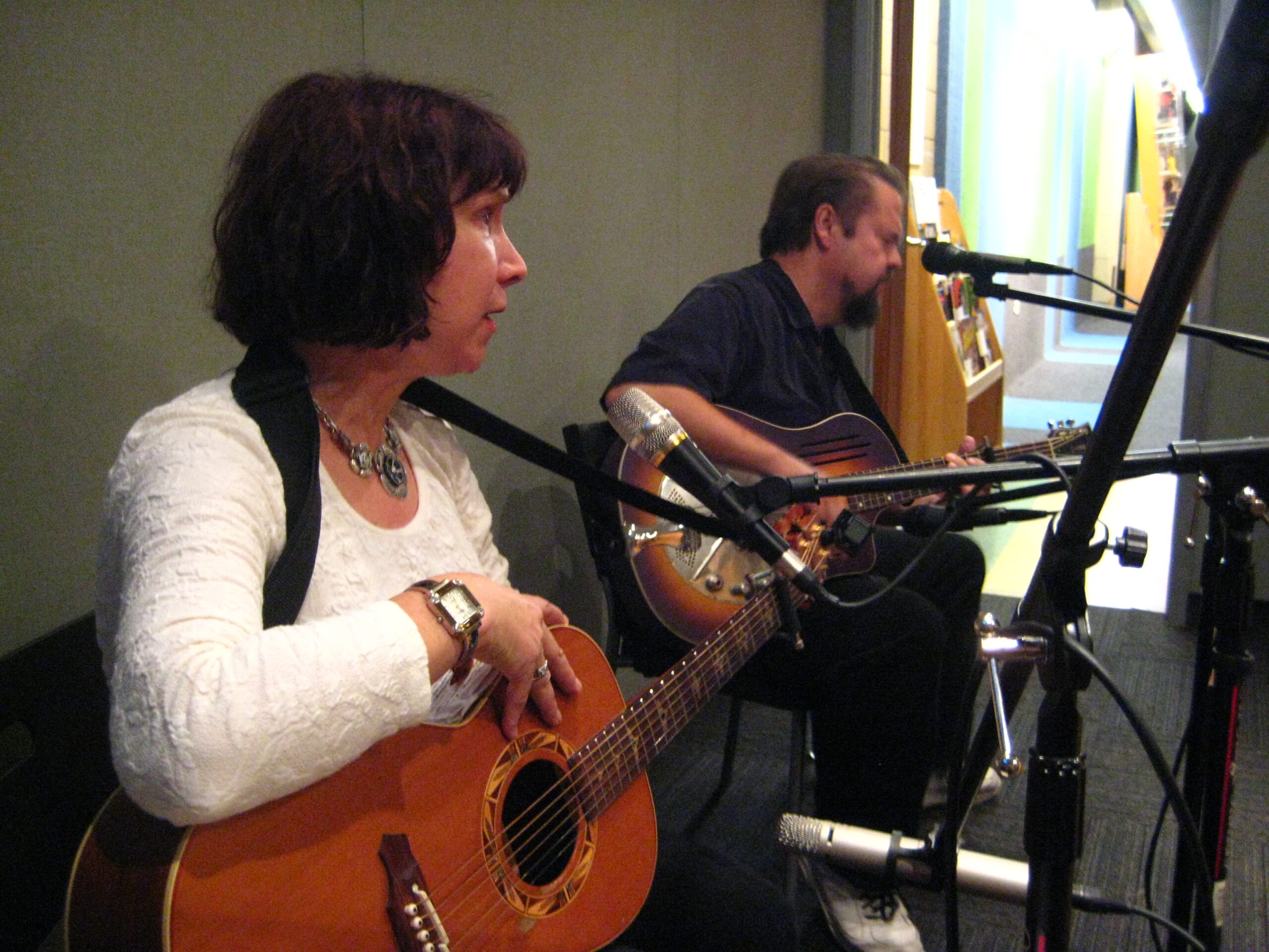 An adult playing an acoustic guitar and an adult playing a dobro in a radio studio