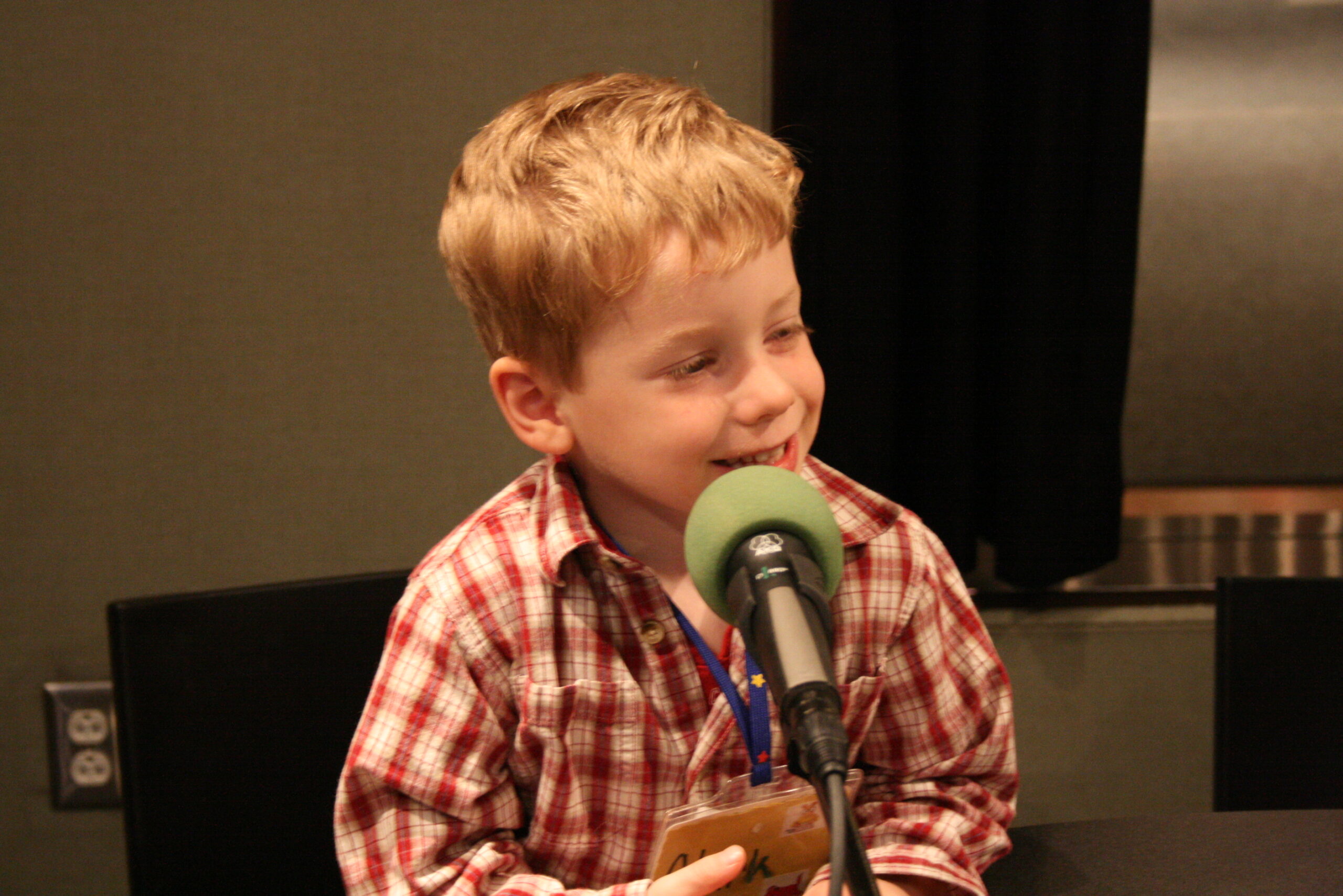 A youth smiling while sitting behind a microphone in a radio studio
