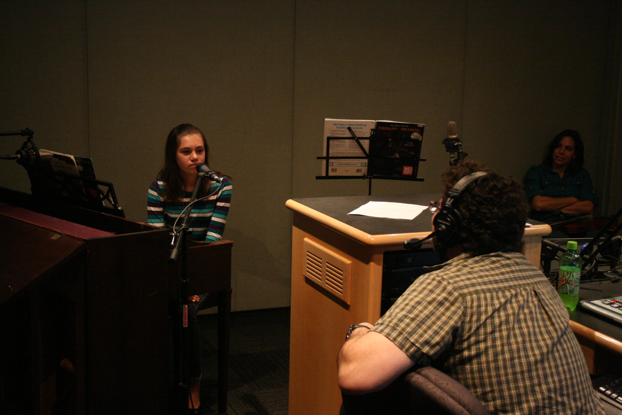 A youth sitting behind a piano keyboard being interviewed by an adult wearing headphones in a radio studio
