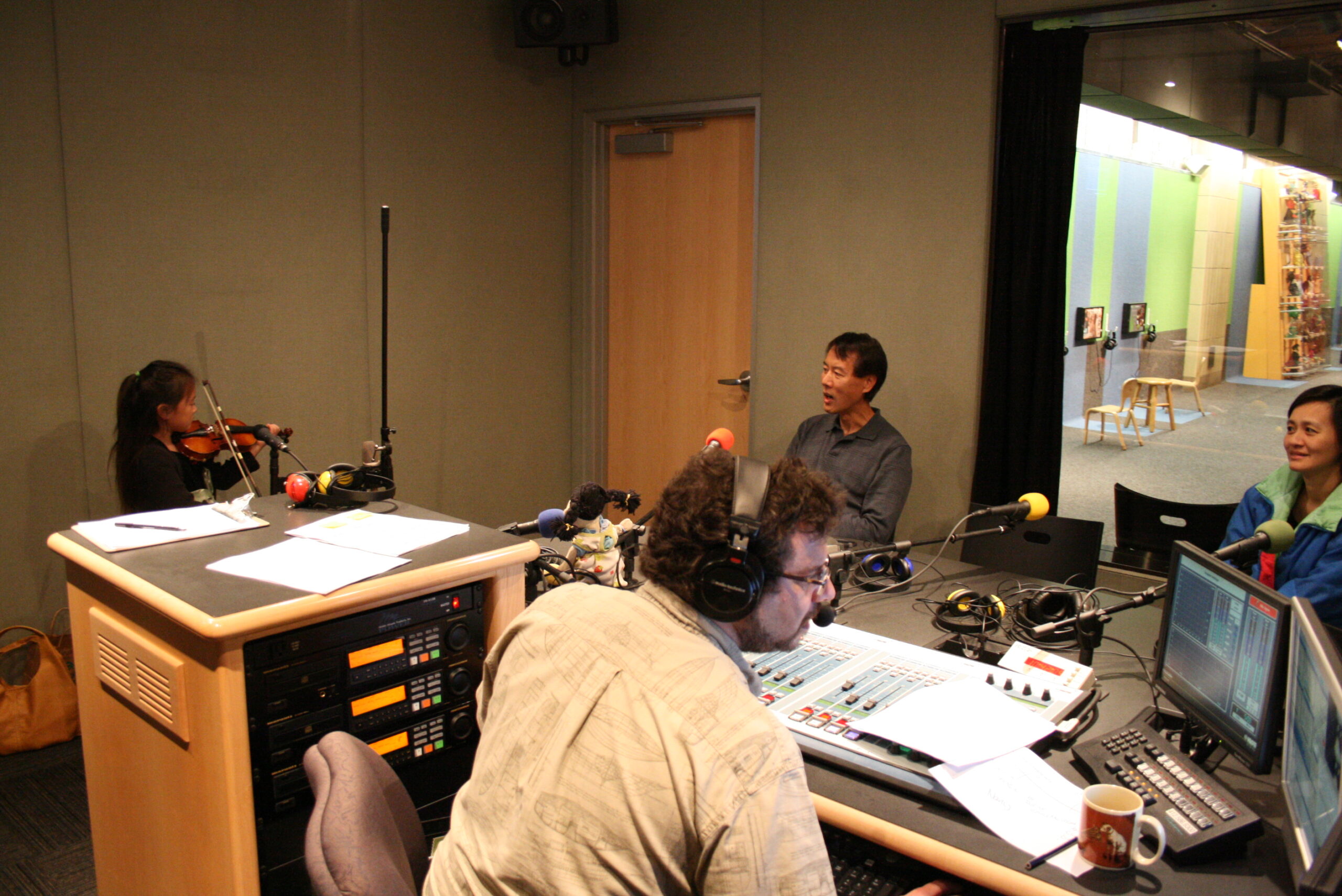 A youth playing a violin as three adults listen in a radio studio