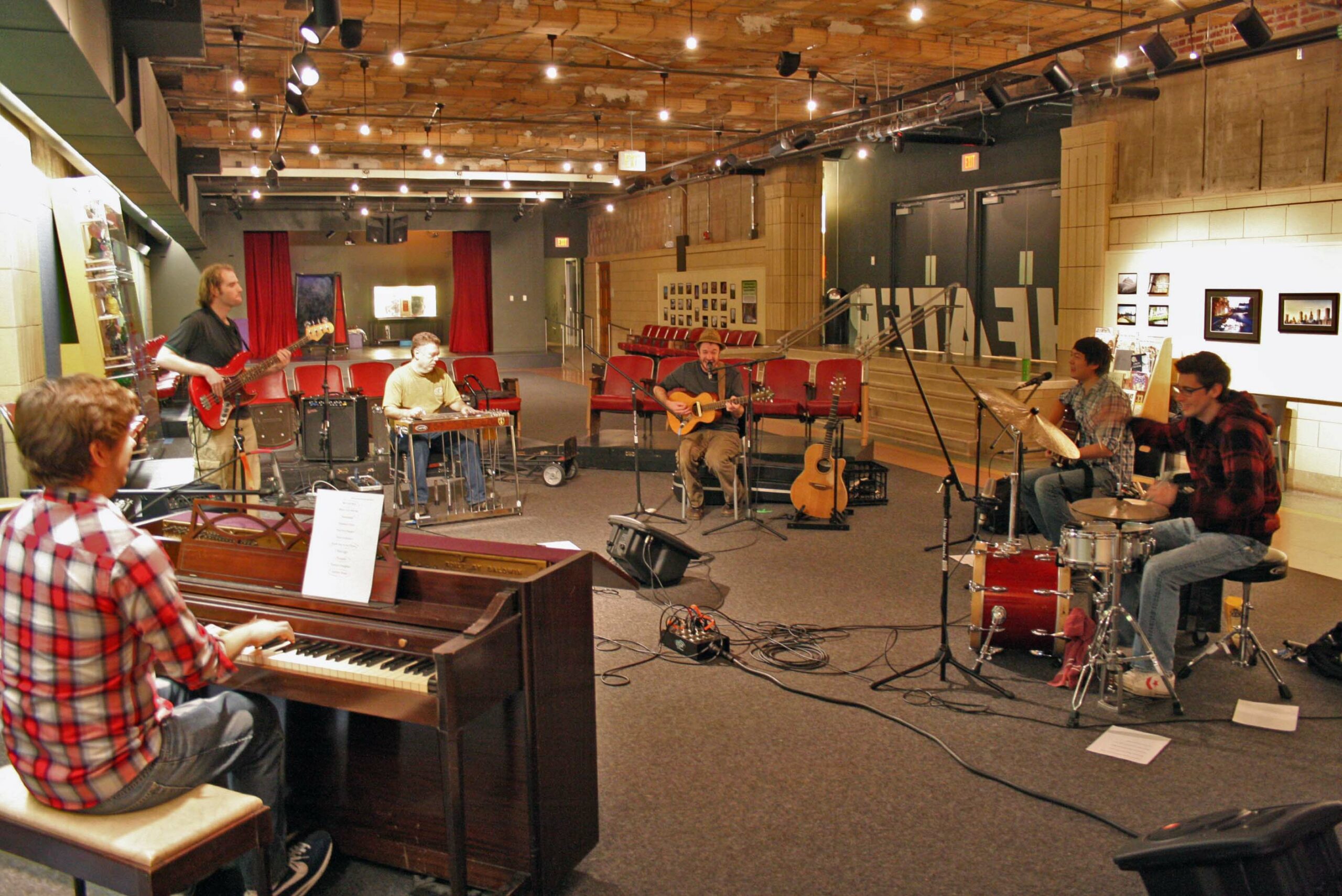 An adult playing a piano, an adult playing an electric bass, an adult playing a pedal steel guitar, an adult playing an acoustic guitar, and an adult playing a drum set