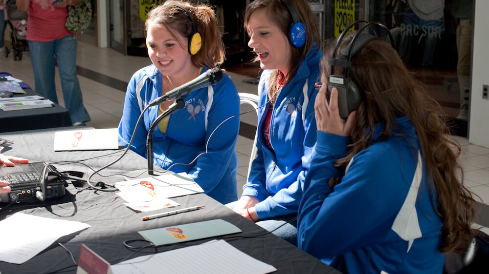 Three youth wearing headphones sitting behind a microphone