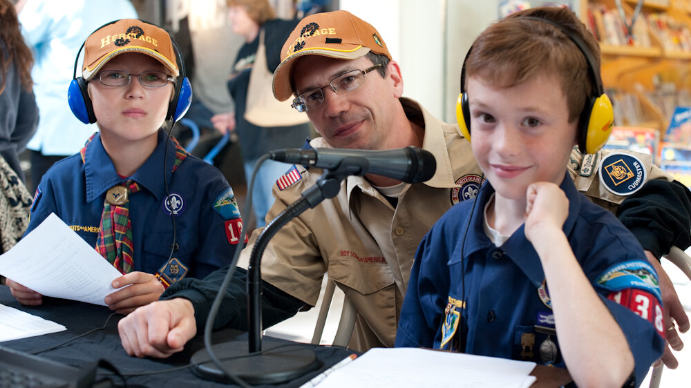 Two youth wearing headphones and an adult sitting behind a microphone