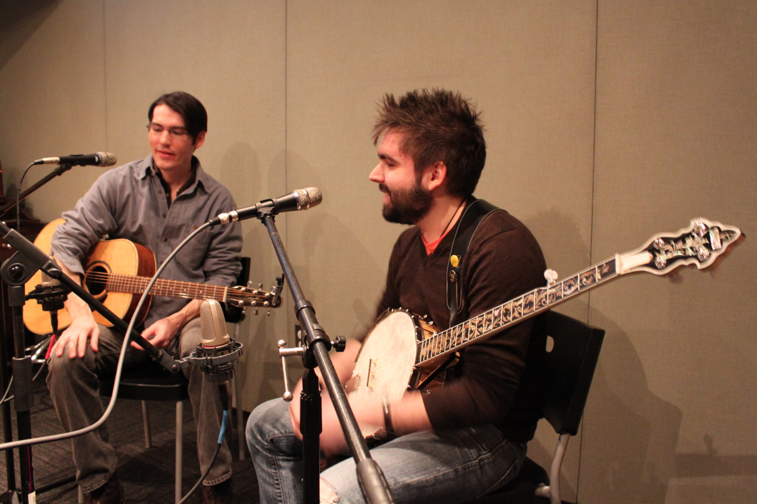 An adult holding an acoustic guitar and an adult holding a banjo in a radio studio