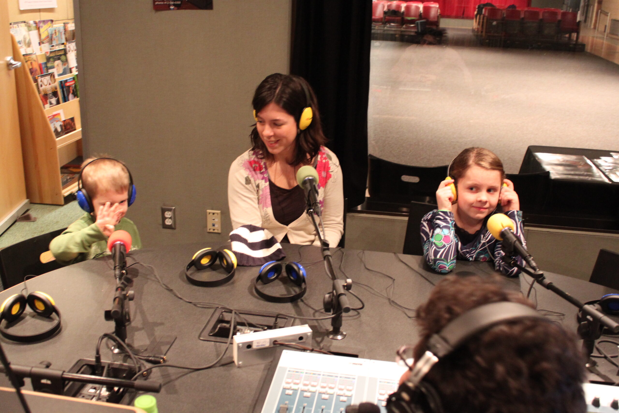 Two youth and an adult wearing headphones sitting behind microphones being interviewed in a radio studio