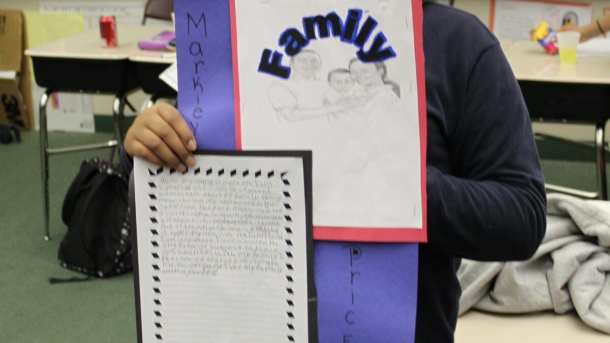 A youth holding a dark blue posterboard in a classroom
