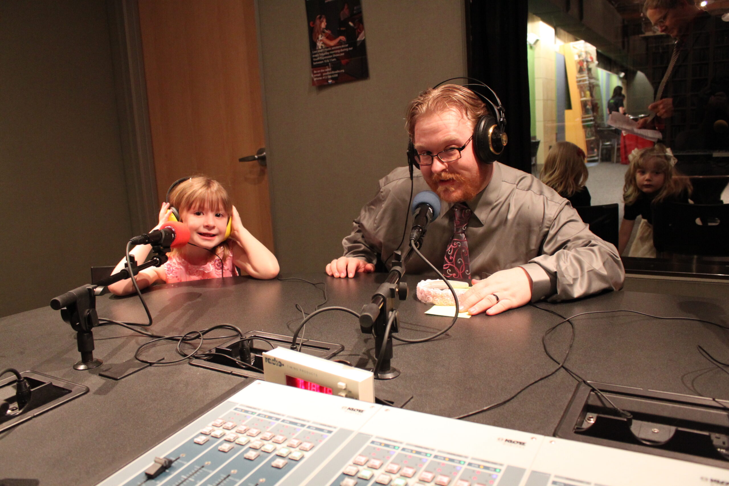 A youth and an adult wearing headphones speaking into microphones in a radio studio