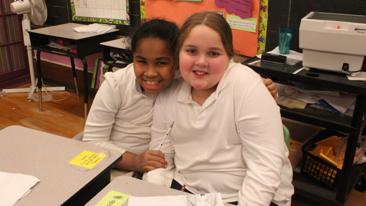 Two youth smiling while sitting at classroom desks