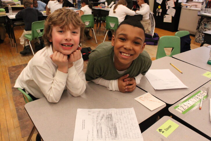Two youth smiling while sitting at a classroom desk