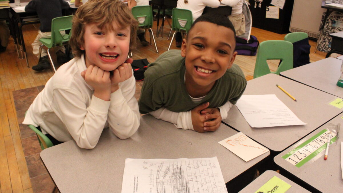 Two youth smiling while sitting at a classroom desk