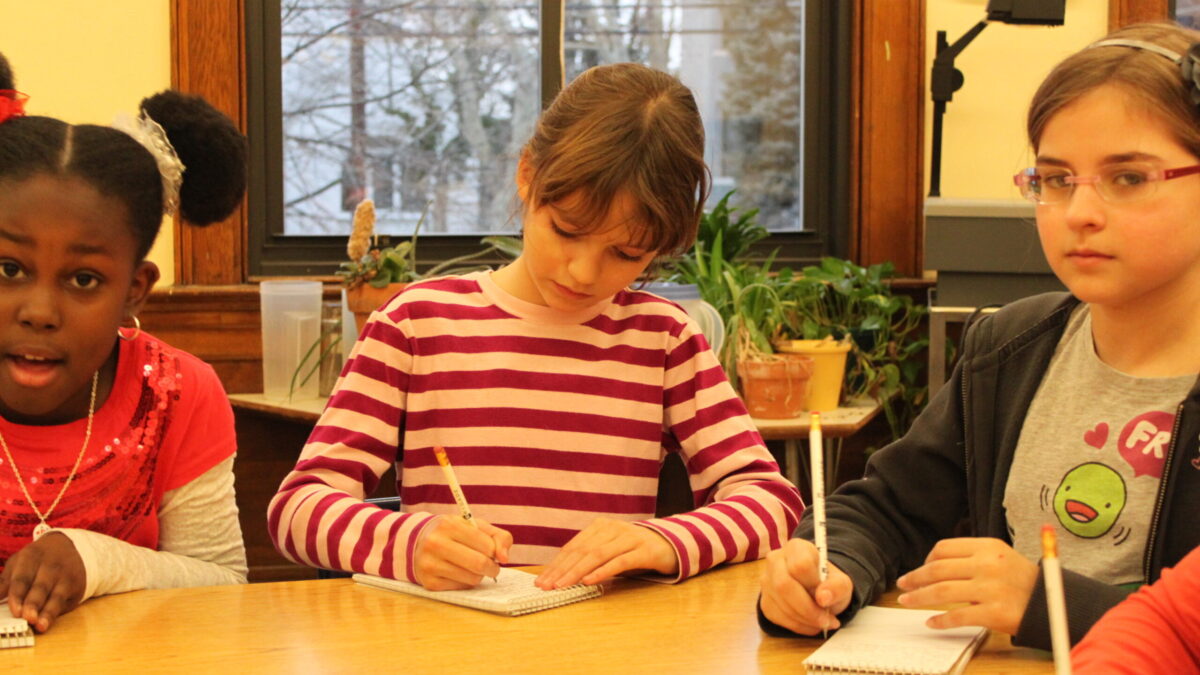 Three youth writing on pieces of paper in a classroom