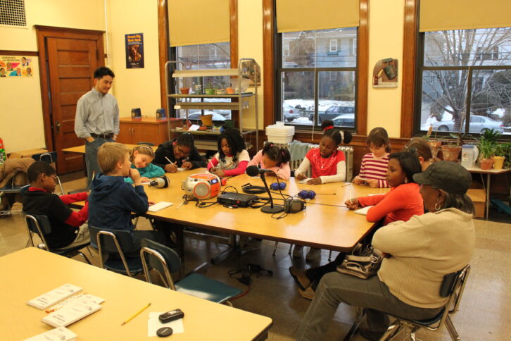 Ten youth and two adults around a table in a classroom