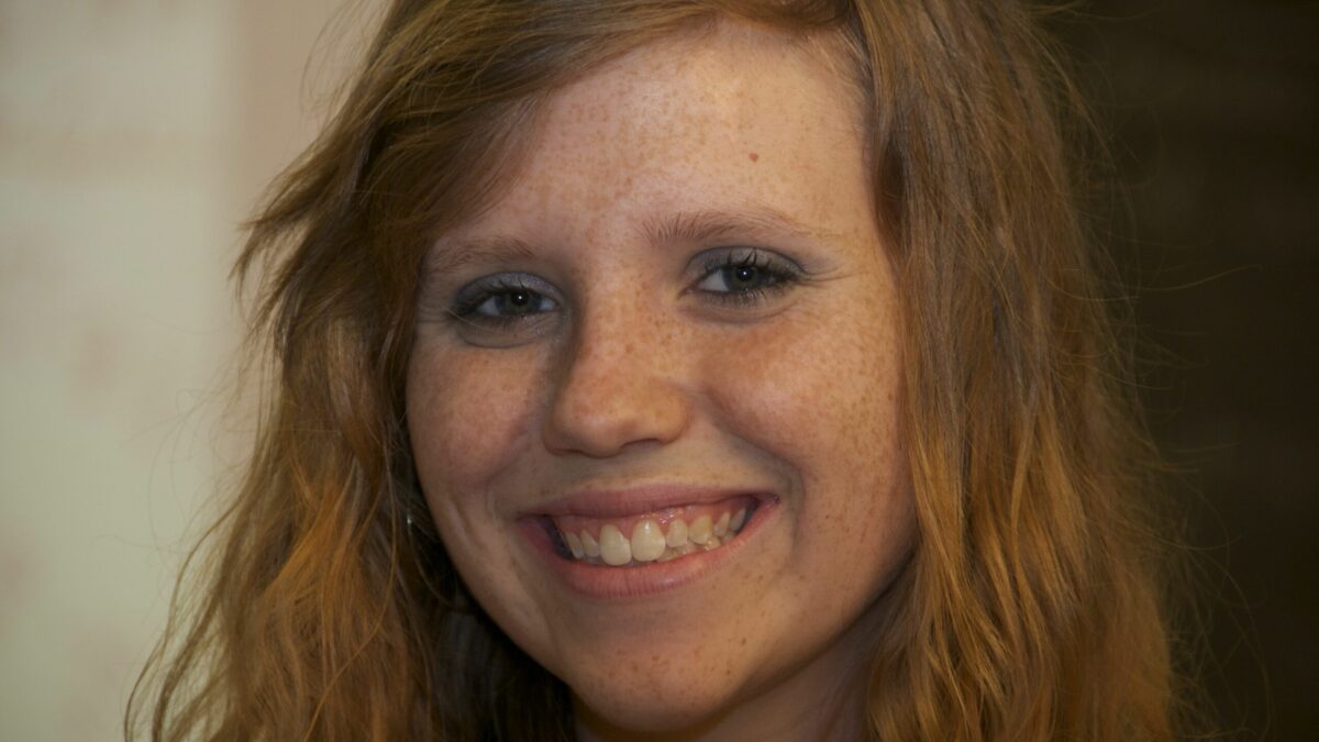 A teen with long reddish-brown hair smiling at the camera