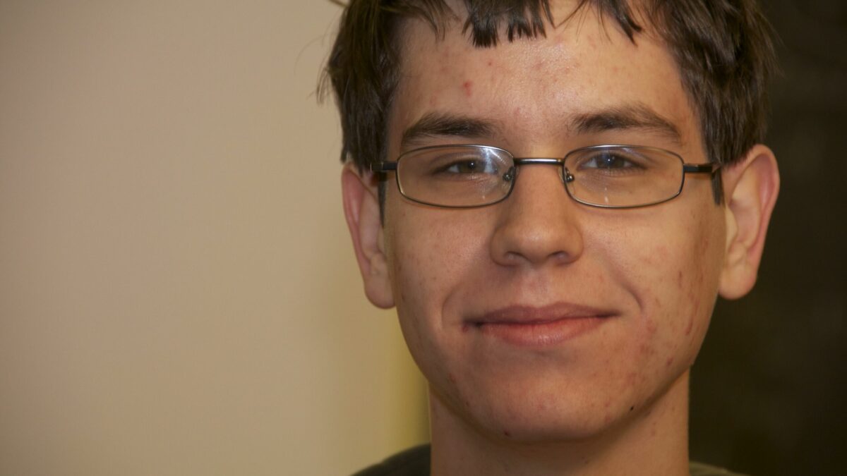 A teen with short brown hair and glasses