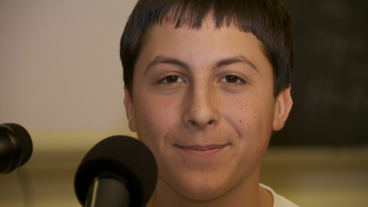 A teenager with short brown hair smiling behind a microphone