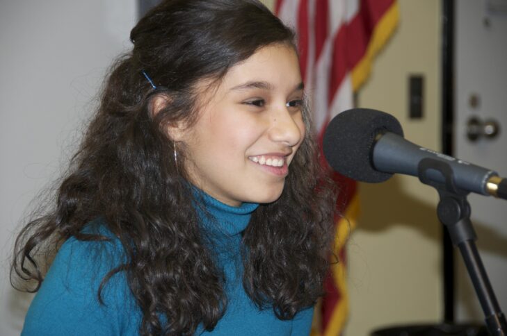 A teen smiling and sitting behind a microphone