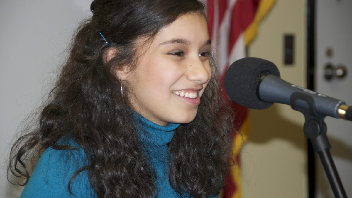 A teen smiling and sitting behind a microphone