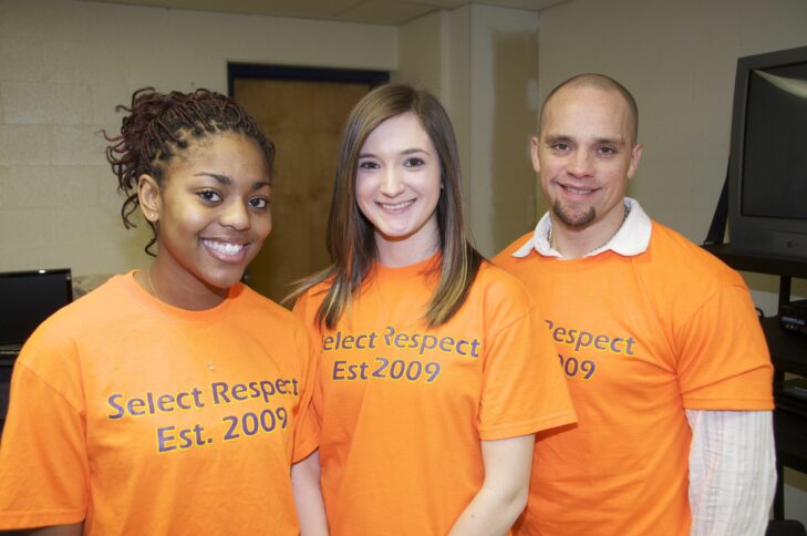 Three teens smiling and wearing orange shirts with the text "Select Respect Est. 2009" on them