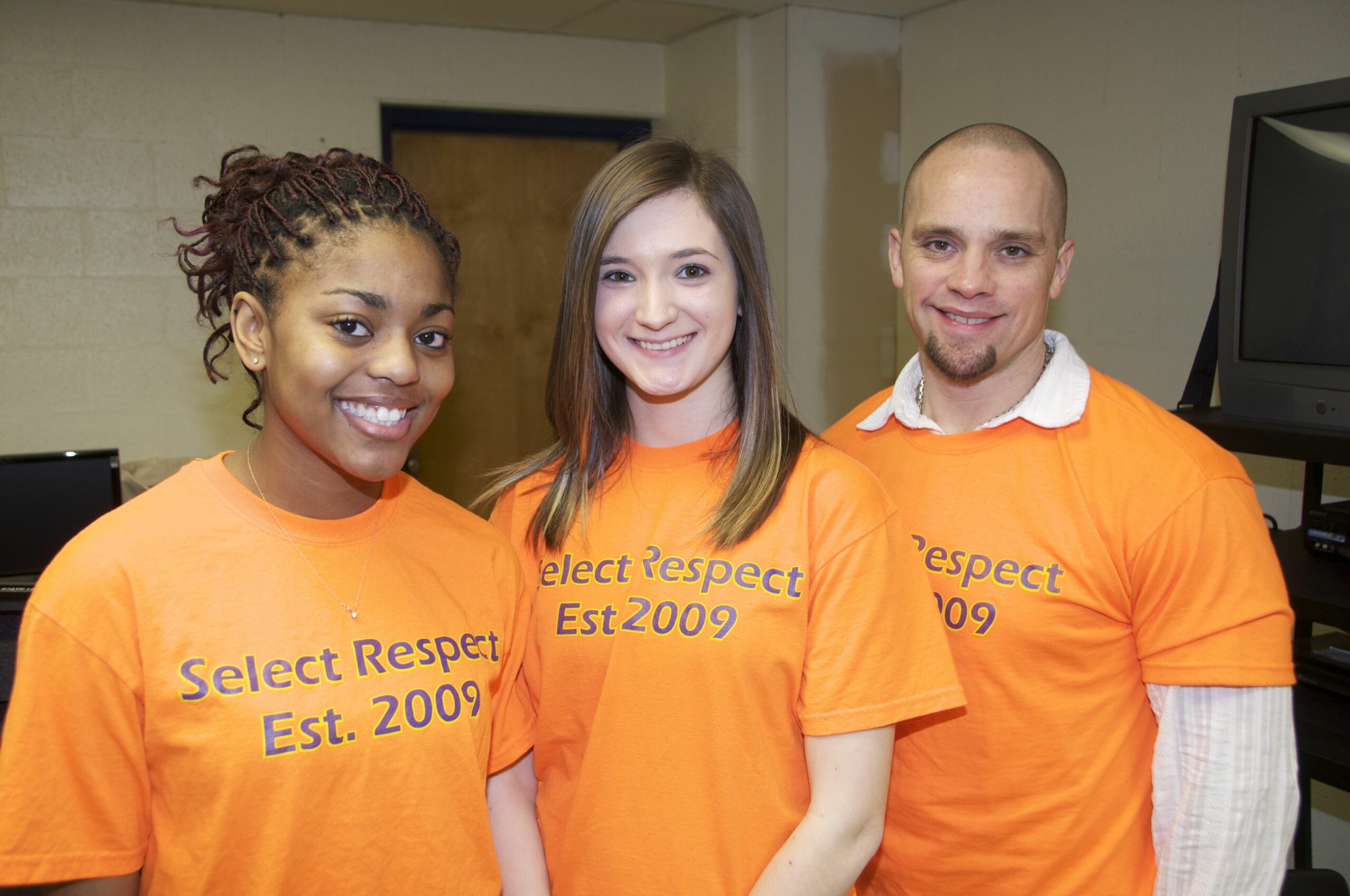 Three teens smiling and wearing orange shirts with the text "Select Respect Est. 2009" on them