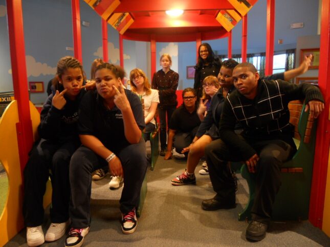 Ten youth smiling and posing near red pillars in a blue room