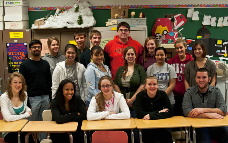 Seventeen teens smiling and posing in a classroom